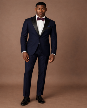 Man wearing a navy blue tuxedo with a white shirt and black shoes on a brown background
